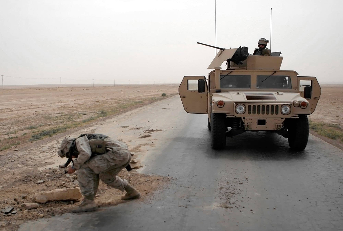 Military Hummer parked on the road with a soldier inspecting a hole in the road